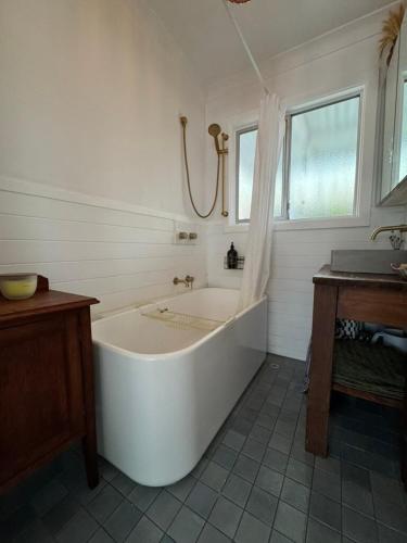 a large white tub in a bathroom with a window at Manaia - A little bach near the beach in Moruya Heads