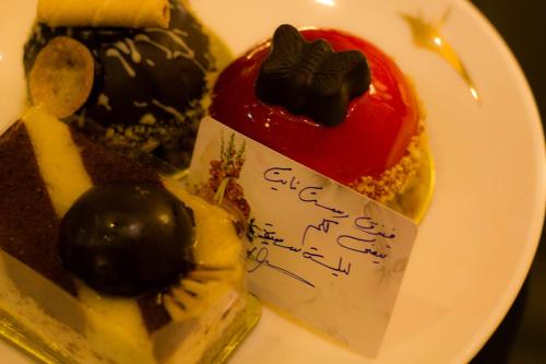a white plate with a piece of cake with cherries on it at Rest Night Serviced Apartments- AlHamra in Riyadh