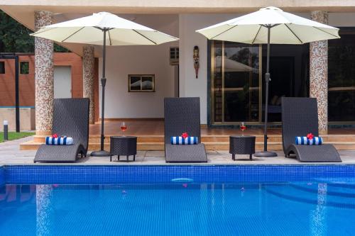 a group of chairs with umbrellas next to a pool at Classique Woods by StayVista with Lawn with Gazebo & Bar, Indoor Fun in Karjat
