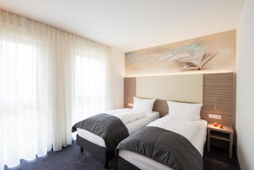two beds in a room with white walls and windows at Book Hotel Leipzig in Leipzig