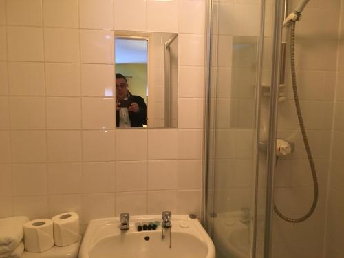 a man taking a picture of a bathroom with a sink and shower at Dukes Head Inn in Richmond upon Thames