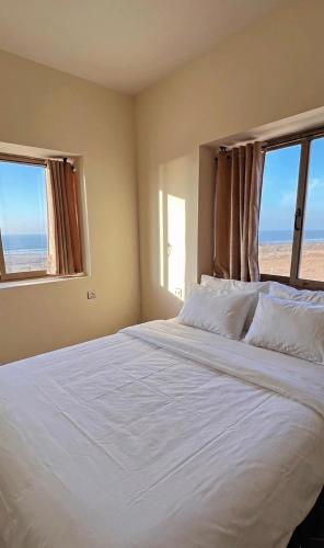 a bedroom with a large white bed with two windows at Tazgha house in Essaouira