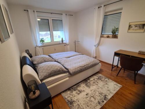 a bedroom with a bed and a desk and two windows at Ferienwohnung Oskar in Gschwend