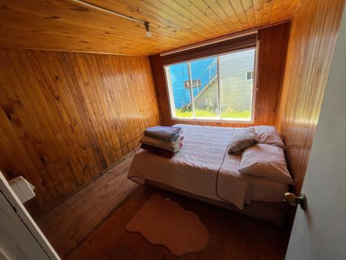 a bedroom with a bed in a wooden room with a window at Cabañas centro Quellón in Quellón
