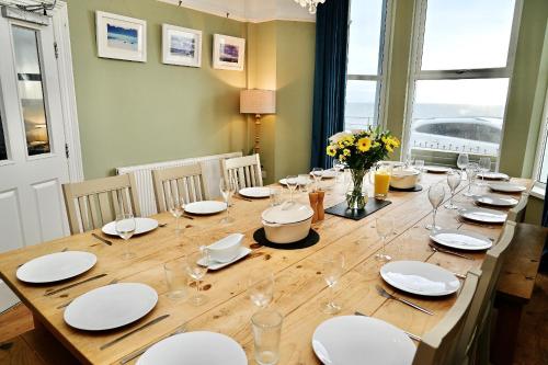 a long wooden table with white plates and wine glasses at Bay View, Sleeps 18, 7 Bedrooms, 7 Bathrooms, Seafront, Criccieth in Criccieth