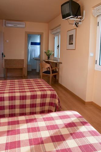 a room with two beds and a tv on the wall at Hotel Villa de Ayerbe in Ayerbe