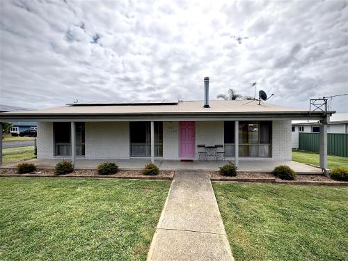 a white house with a pink door and grass at Shell Shack in Tomakin