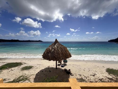 a straw umbrella on a beach with the ocean at Beach front luxury living - 2 bedroom condo with sea view in Jan Thiel