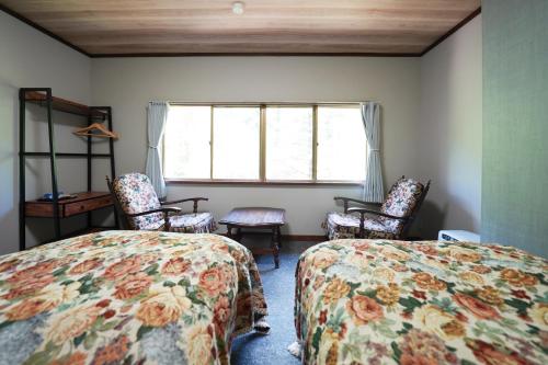 a bedroom with two beds and chairs and a window at Yamano Hidaya in Matsumoto