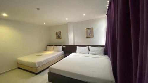 two beds in a hotel room with purple curtains at Hotel Vistana Micassa in Taiping