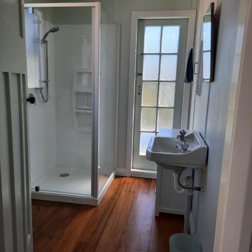 a bathroom with a glass shower and a sink at Little Blue Bach in Whanganui
