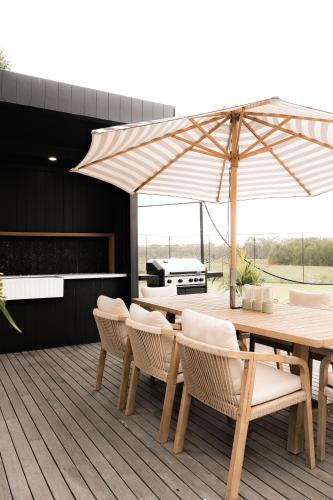 a wooden table with chairs and an umbrella on a deck at The Station Hunter Valley in Pokolbin