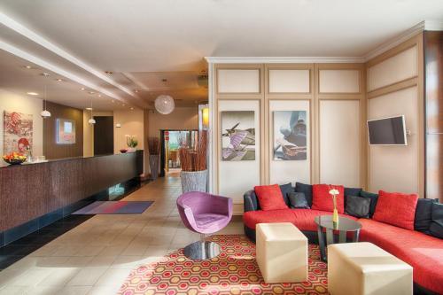 a living room with a red couch and a pink chair at Leonardo Hotel Köln Bonn Airport in Cologne