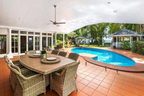 a patio with a table and chairs and a pool at Willow Garden Stays Cairns - Beachfront 4 Bedroom Luxury Holiday Home in Kewarra Beach
