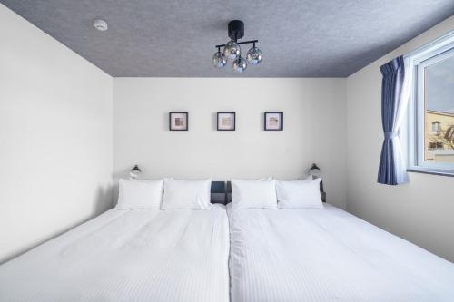 a white bedroom with two beds and a window at Hills Niseko 105 in Niseko