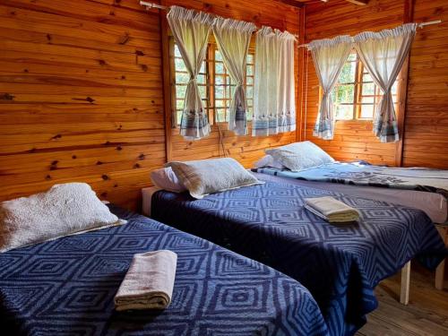 two beds in a wooden room with windows at Backpackers at Kanaan in Hazyview