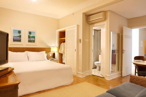 a bedroom with a white bed and a bathroom at Vitória Hotel Concept Campinas in Campinas
