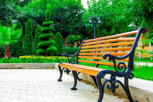 a wooden bench sitting on a sidewalk in a park at Vilesh Palace Hotel in Masallı