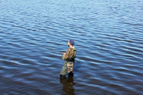 a boy standing in the water holding a fishing rod at Hotel Højbysø in Højby