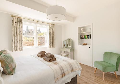 a white bedroom with a bed and a green chair at Lochburn Cottage in Elie