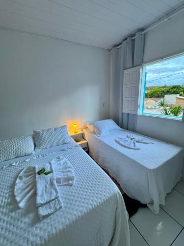 a white bedroom with two beds and a window at Casa Dona Vera - Seu Refúgio no Centro Histórico in Mucugê