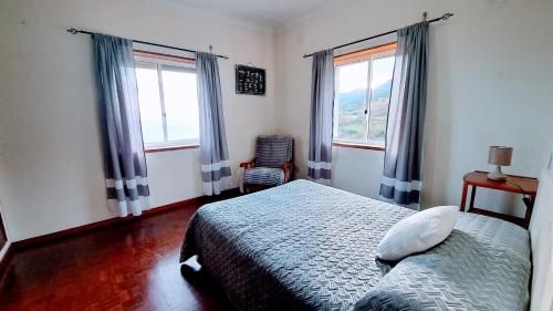 a bedroom with a bed and two windows and a chair at Casa da Maíssa in Ponta Delgada