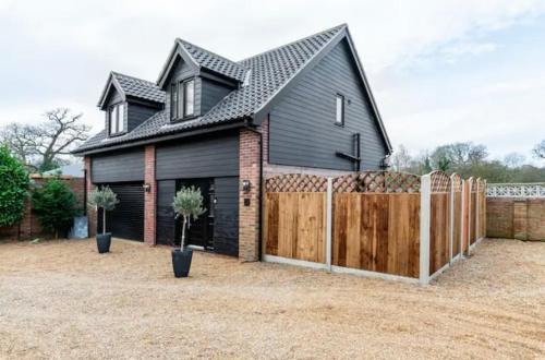 a black house with a wooden fence in a yard at Stargazing Filby, Norfolk Guest House in Great Yarmouth