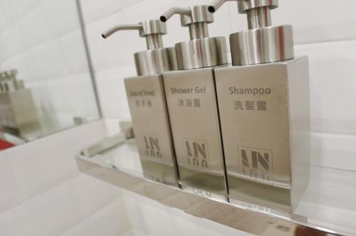 Un estante con tres dispensadores de jabón en un baño. en In Inn, en Hong Kong