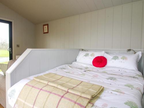 a bed with a red pillow on top of it at Leafy Oaks Cabin in Much Wenlock