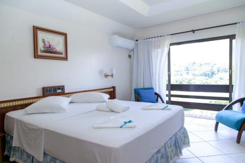 a bedroom with a large white bed and a large window at Tureck Garten Hotel in Corupá