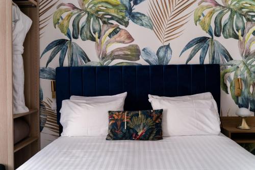 a bed with a blue headboard with a tropical wallpaper at Hotel Boileau in Paris