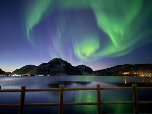 an aurora over a body of water with a fence at Modern seafront cabin with sauna 8 mins to Leknes in Storeidet