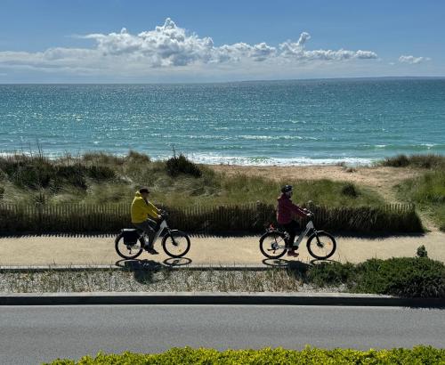 two people riding bikes down a road near the ocean at Villa Denise Petit Gîte in Barneville-Carteret