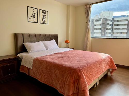 a bedroom with a bed with a red blanket and a window at Amplia suite cerca a La Carolina - Av 6 Diciembre in Quito