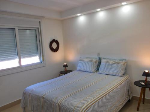 a white bedroom with a bed with two windows at Buenos Aires 705 in Osório