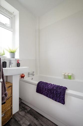 a white bathroom with a purple towel on a tub at Cheerful and Cosy Double Room in Belfast