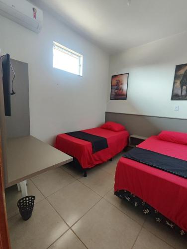 a room with two beds with red sheets and a window at Quarto Duplo Comercial - Queen's Hotel in Formosa