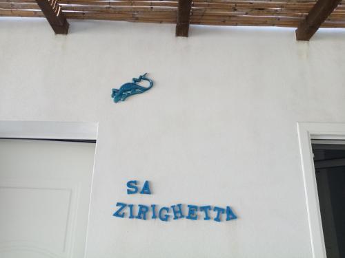 a sign on the side of a white wall with a lizard on it at Sa Zirighetta in S'archittu Cuglieri