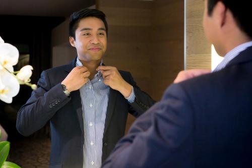 a man adjusting his tie in front of a mirror at Pullman Sydney Airport in Sydney