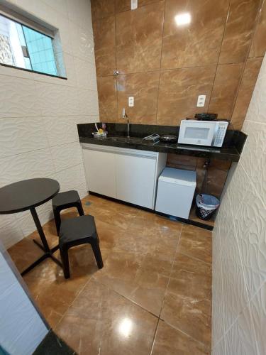 a kitchen with a counter and a table and a microwave at Suíte Família 5 pessoas - Queen's Hotel in Formosa