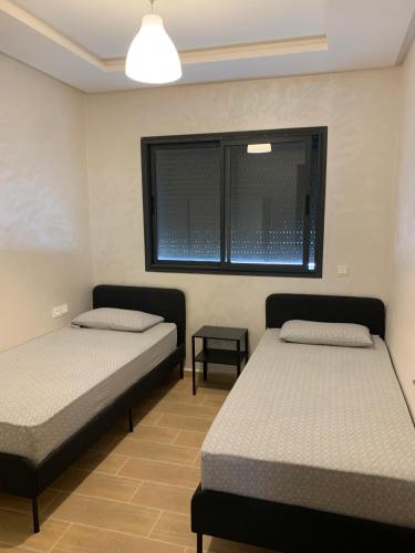two beds in a room with a window at bel appartement juste à côté de McDonald's in Kenitra