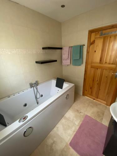 a white bath tub in a bathroom with a door at Rockside Villa Cashel Sleeps 6, Jacuzzi Bath, Walk to Rock of Cashel in Cashel
