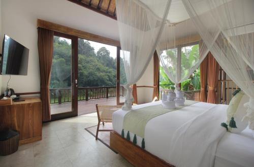 a bedroom with a bed and a television and a balcony at The Tirta Sari Villas in Tegalalang