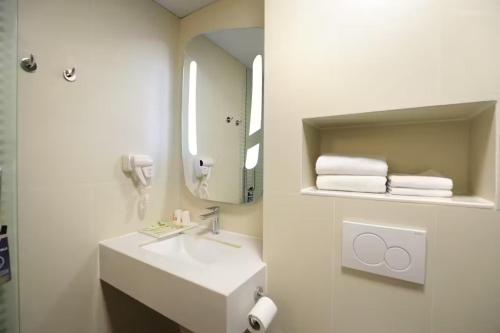 a white bathroom with a sink and a mirror at Ibis Dujiangyan in Dujiangyan