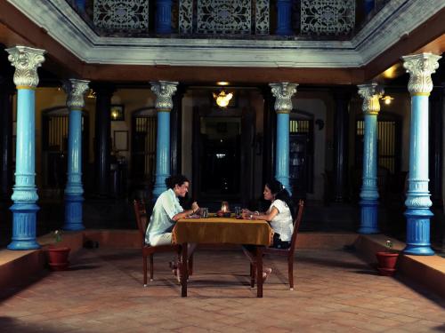 a man and woman sitting at a table in a building at Chettinadu Mansion – An Authentic Heritage Palace in Kānādukāttān