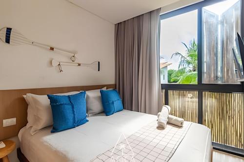 a bedroom with a bed with blue pillows and a window at Aluá Patacho in Pôrto de Pedras