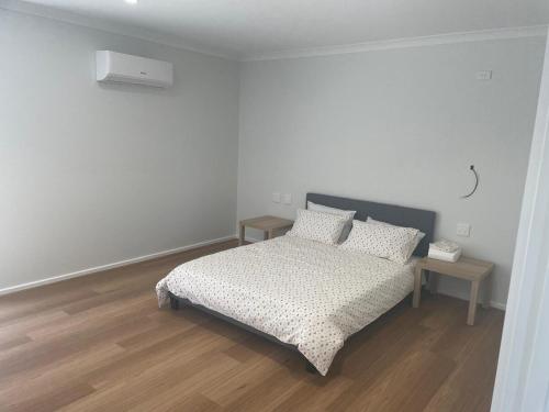 a white bedroom with a bed and two tables at Southern Retreat in Clyde North