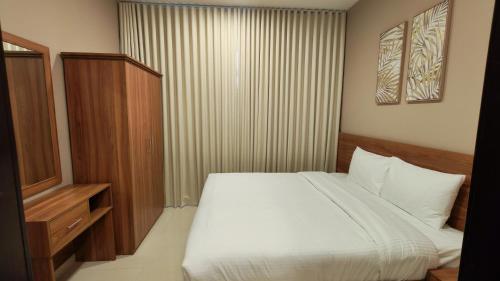 a bedroom with a white bed and a wooden cabinet at Al Khaleej Plaza Furnished Hotel Apartments in Ajman 