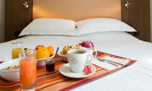a tray of breakfast foods and drinks on a bed at Brit Hotel Le Kerann Nantes St Herblain - Zac De La Lorie in Saint-Herblain