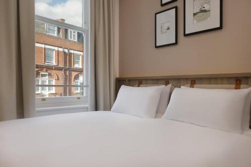 a bed with white pillows in front of a window at The Drey - Kensington, Earl's Court in London
